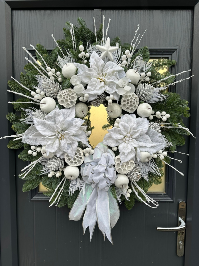 Silver Christmas Wreath - Transform your entrance into a magical winter scene with the Winter Wonderland Christmas Wreath. Handcrafted with fresh evergreen foliage, this elegant design features frosted seasonal accents, snowy berries, decorative ornaments, natural textures, and shimmering details, all beautifully finished with a luxurious iridescent bow. Its crisp white and silver palette creates a sophisticated, snow-kissed look, making it the perfect statement wreath for a classic and elegant Christmas display.