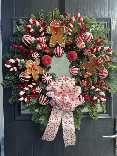 Gingerbread Lane - Fill your home with festive fun using the Gingerbread Lane Christmas Wreath. Handcrafted with fresh evergreen foliage, this cheerful design is adorned with candy cane decorations, playful gingerbread characters, festive baubles, seasonal berries, decorative apples, charming bird ornaments, and a luxurious candy cane-patterned bow. Bursting with colour and nostalgic Christmas charm, this delightful wreath is the perfect way to create a warm and joyful welcome throughout the festive season.