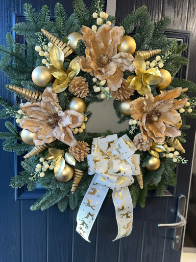 Golden Elegance - Celebrate the season with the luxurious charm of the Golden Elegance Christmas Wreath. Handcrafted with fresh evergreen foliage, this stunning design features shimmering gold accents, champagne baubles, frosted pinecones, delicate ivory berry sprays, and a beautifully finished ivory ribbon adorned with elegant gold reindeer. Rich in warm metallic tones and festive textures, this wreath brings timeless sophistication to any front door and makes a striking statement throughout the Christmas season.