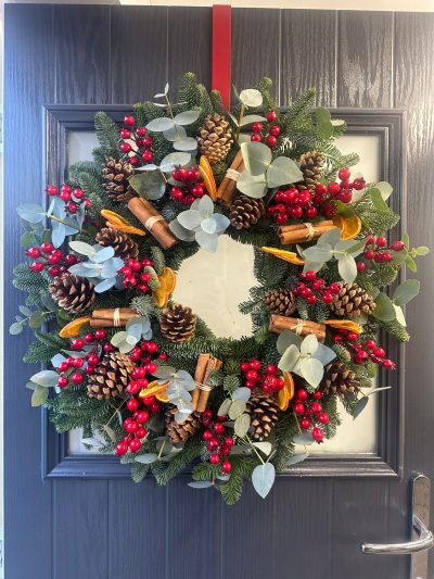 Woodland Spice - Bring the beauty of a traditional woodland Christmas to your home with the Woodland Spice Christmas Wreath. Handcrafted with fresh evergreen foliage, this natural design features eucalyptus, vibrant red berry accents, pinecones, aromatic cinnamon bundles, and dried orange slices for a warm, rustic finish. Rich in seasonal textures and classic festive colours, this elegant wreath creates a welcoming display that perfectly captures the cosy spirit of Christmas.